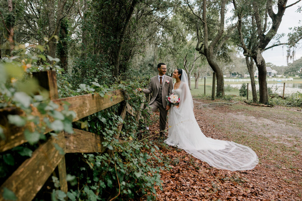 Bride and groom under the oaks by a wooden fence at Bridlewood Ranch